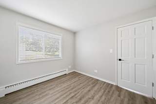 A room with a white door, window with blinds, and a radiator on the wall.