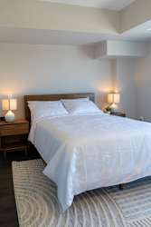 A bed with white bedding sits in a room with two lamps on either side of it.