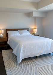 A bed with white bedding sits in a room with a striped rug.