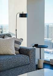 A grey couch with a white pillow and a black table with a lamp on it.