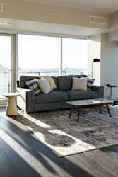 A grey couch with pillows and a small table in front of a large window.