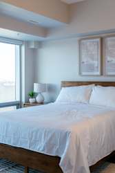 A bed with white bedding sits in a room with a window.