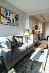 A grey couch with a white pillow is in the middle of a room with a painting on the wall.