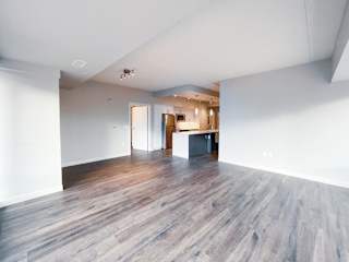 an empty living room with hardwood floors and a kitchen in the background