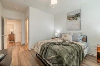 A bedroom with a bed covered in a green blanket and a painting hanging on the wall.