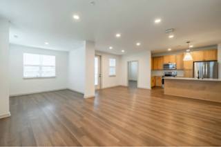 A spacious room with wooden floors and a kitchen area in the background.