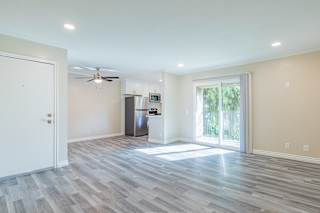 an empty living room with a sliding glass door and a kitchen in the background