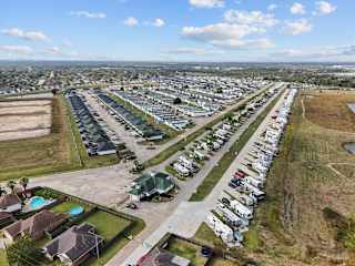 A large parking lot with numerous cars and a few houses in the background.