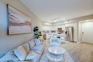 A living room with a white couch and a painting on the wall.