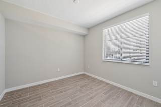 A room with a window covered by white blinds and wooden flooring.