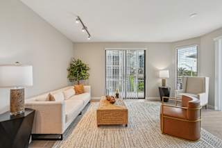A living room with a white couch, a wooden coffee table, and a large window with a view of the outside.