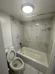 A white toilet is next to a bathtub in a marble bathroom.