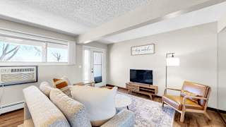 A living room with a white couch, a wooden chair, and a television on a stand.