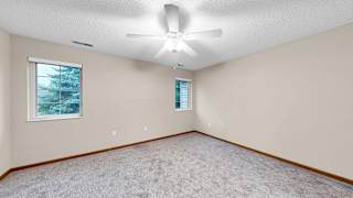 A room with a ceiling fan and two windows.