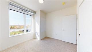 A room with a carpeted floor, a window with blinds, and a door at The Bessemer at Seward Commons Apartments, Minneapolis