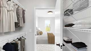 A white closet with clothes hanging and a doorway leading to a bedroom.