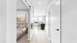 A white hallway with a bedroom and a kitchen visible through the door.
