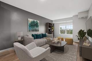 A living room with a grey couch, a grey armchair, a coffee table, a lamp, a book, a plant, and a painting on the wall.