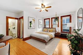 A bedroom with a bed, a ceiling fan, and a potted plant.