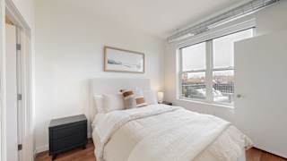 A bedroom with a large bed, a nightstand, and a window overlooking a cityscape.at Tyler Street Stacks, Minneapolis, MN