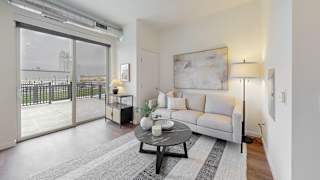 A living room with a grey couch, a coffee table, and a large window with a view of a cityscape. at Tyler Street Stacks, Minneapolis, MN 55413