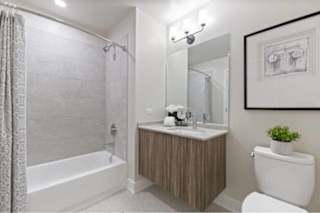 A bathroom with a white toilet, a bathtub with a shower curtain, a sink with a mirror, and a framed picture on the wall.