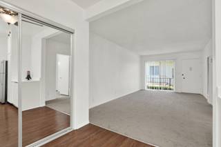 a living room with white walls and a mirrored door at Olive Tree Apartments, Torrance, CA