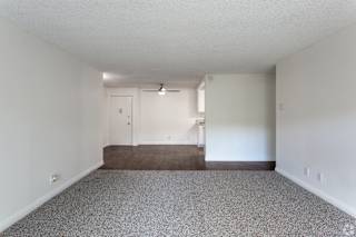 an empty living room with carpet and white walls at Willow Tree Apartments, California