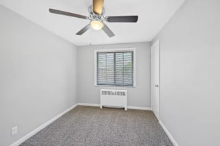 A room with a ceiling fan, a window with blinds, and a radiator on the wall at Huntley Ridge Apartments, Kettering, OH, 45419
