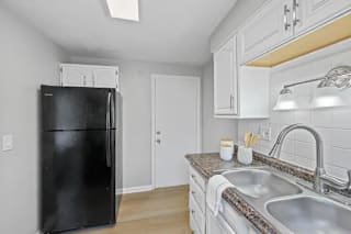 A black refrigerator stands in a kitchen with a sink and cabinets at Huntley Ridge Apartments, Kettering, OH