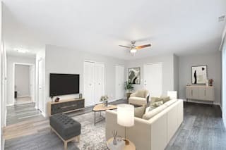 A modern living room with a grey sofa, a grey ottoman, a white coffee table, a white side table, a white lamp, a white TV, a white cabinet, a white rug, a white ceiling fan, and white walls at Parkvie