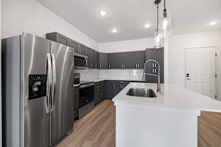 A modern kitchen with a stainless steel refrigerator and wooden floors.