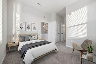 A bedroom with a bed, chair, and potted plant.