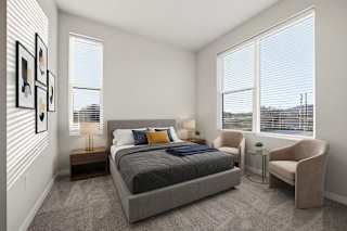 A bedroom with a large bed, a chair, and a window with blinds.
