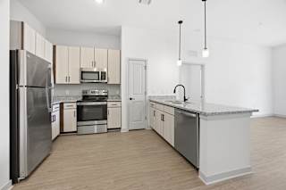 A kitchen with a refrigerator, microwave, oven, sink and cabinets.