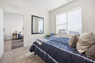 A bedroom with a bed, a mirror, and a window with blinds.