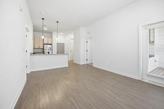 A spacious room with wooden flooring and a kitchen area in the background.