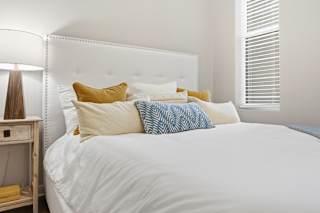 A white bed with a white headboard and a white nightstand with a lamp on it.