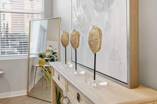 A room with a large painting, a mirror, and three objects on a table.