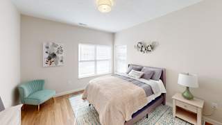 A bedroom with a bed, chair, and lamp at The Landing Apartments, Avon, IN