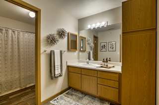 A bathroom with a wooden vanity and a mirror above it. at Tranquility Pointe, Omaha, NE