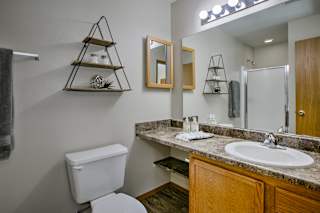 A bathroom with a toilet, sink, mirror, and shelves. at The Pointe, LaVista, Nebraska