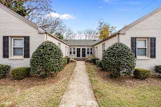 A house with a grey siding and black shutters is surrounded by green bushes.at Raleigh Rentals, Raleigh, NC, 27604