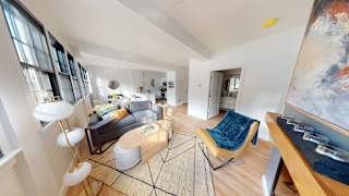 A living room with a rug, a chair, a table, and a painting on the wall.