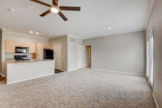 an empty living room with a ceiling fan and a kitchen at Artisan Apartments & Shops, Texas