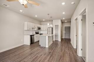 an open kitchen and living room with white walls and wood floors at The Augustan, Augusta, GA