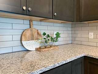 a corner of the kitchen with dark cabinets, a white tile backsplash, and a decorative cutting board
