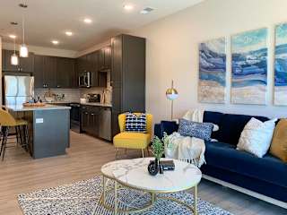 a living room with blue and yellow decor next to a kitchen with dark cabinets