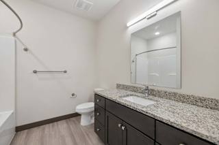 Apartment bathroom with granite countertop, dark vanity, large mirror, toilet, and tub-shower combination.
