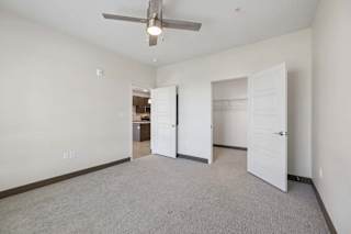 Carpeted apartment bedroom with a ceiling fan, open closet with shelving, and doorway leading to the kitchen.